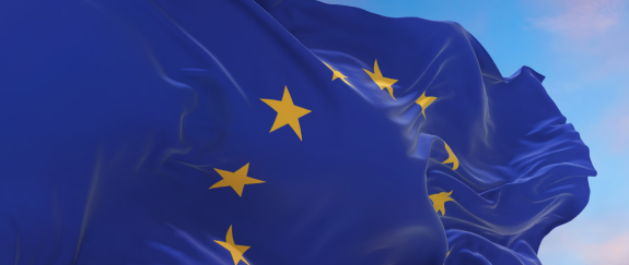Powiewająca flaga Unii Europejskiej na tle wieczornego, lekko zachmurzonego nieba